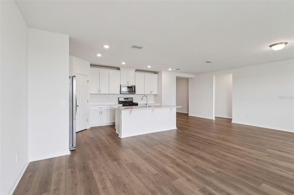 A modern kitchen with white cabinetry and an island opens to a spacious living area — 2867 HORNBILL DRIVE, ST CLOUD, FL