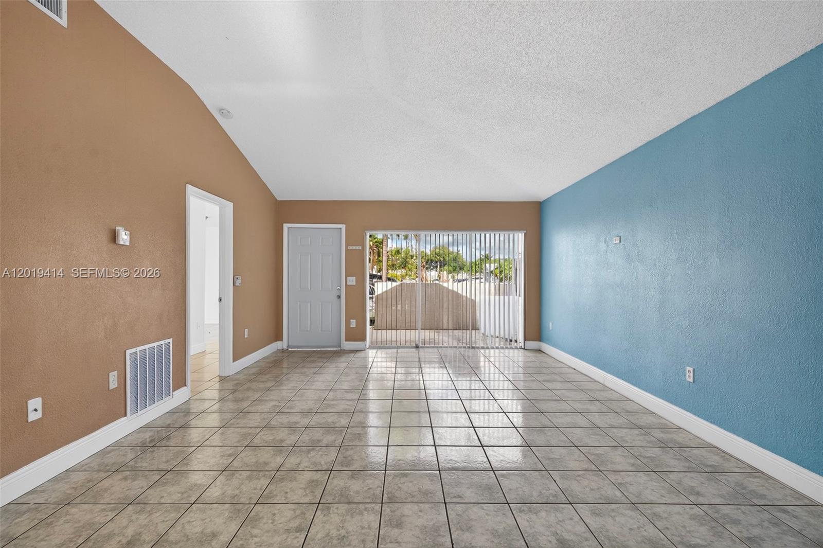 An empty living room features tan and blue walls, tile flooring, and a sliding glass door — 20841 SW 103rd Ct, Cutler Bay FL 33189, CUTLER BAY, FL