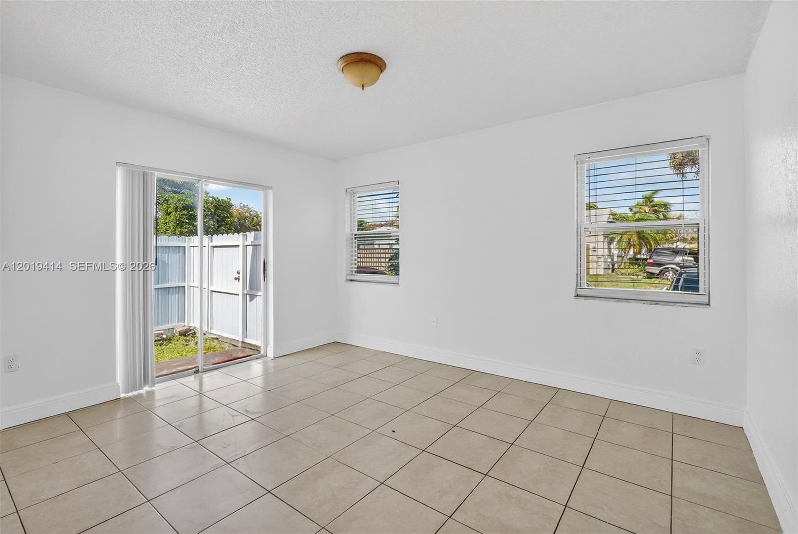 An empty room features white walls, beige tile flooring, two windows, and a sliding door — 20841 SW 103rd Ct, Cutler Bay FL 33189, CUTLER BAY, FL