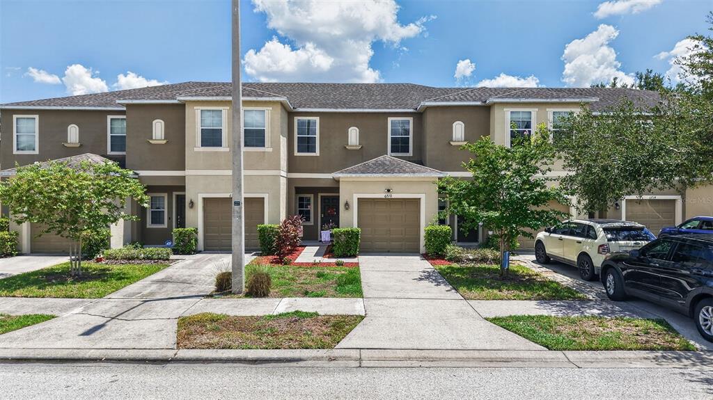 A row of two-story townhouses with attached garages and driveways under a blue sky — 6710 HOLLY HEATH DRIVE, RIVERVIEW, FL