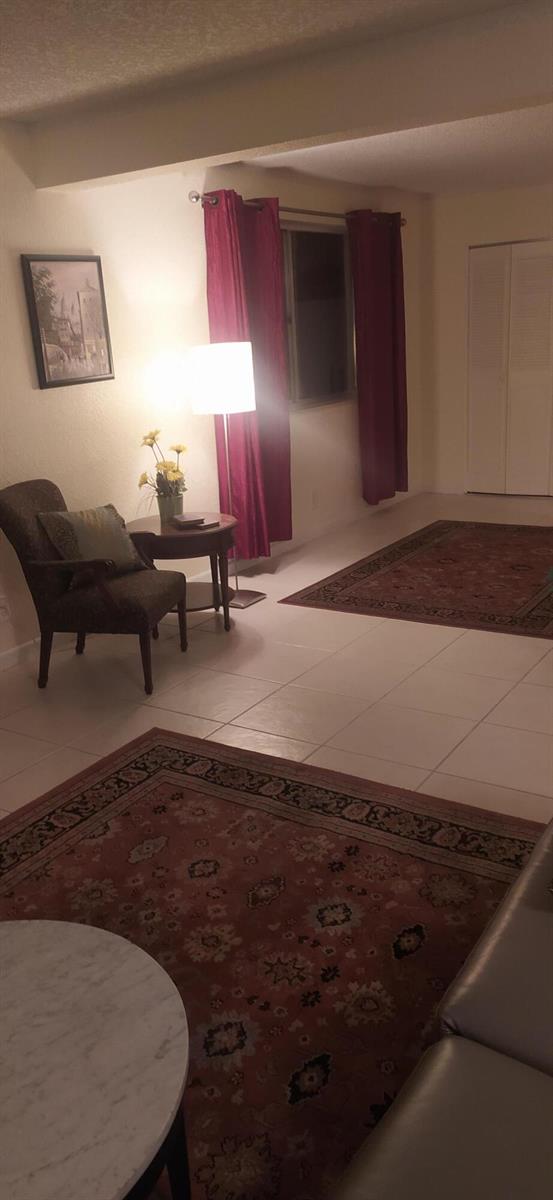 A living room features tile flooring, two area rugs, a dark armchair, and red curtains — 2687 Garden Drive N # 108, FL 33461, FL