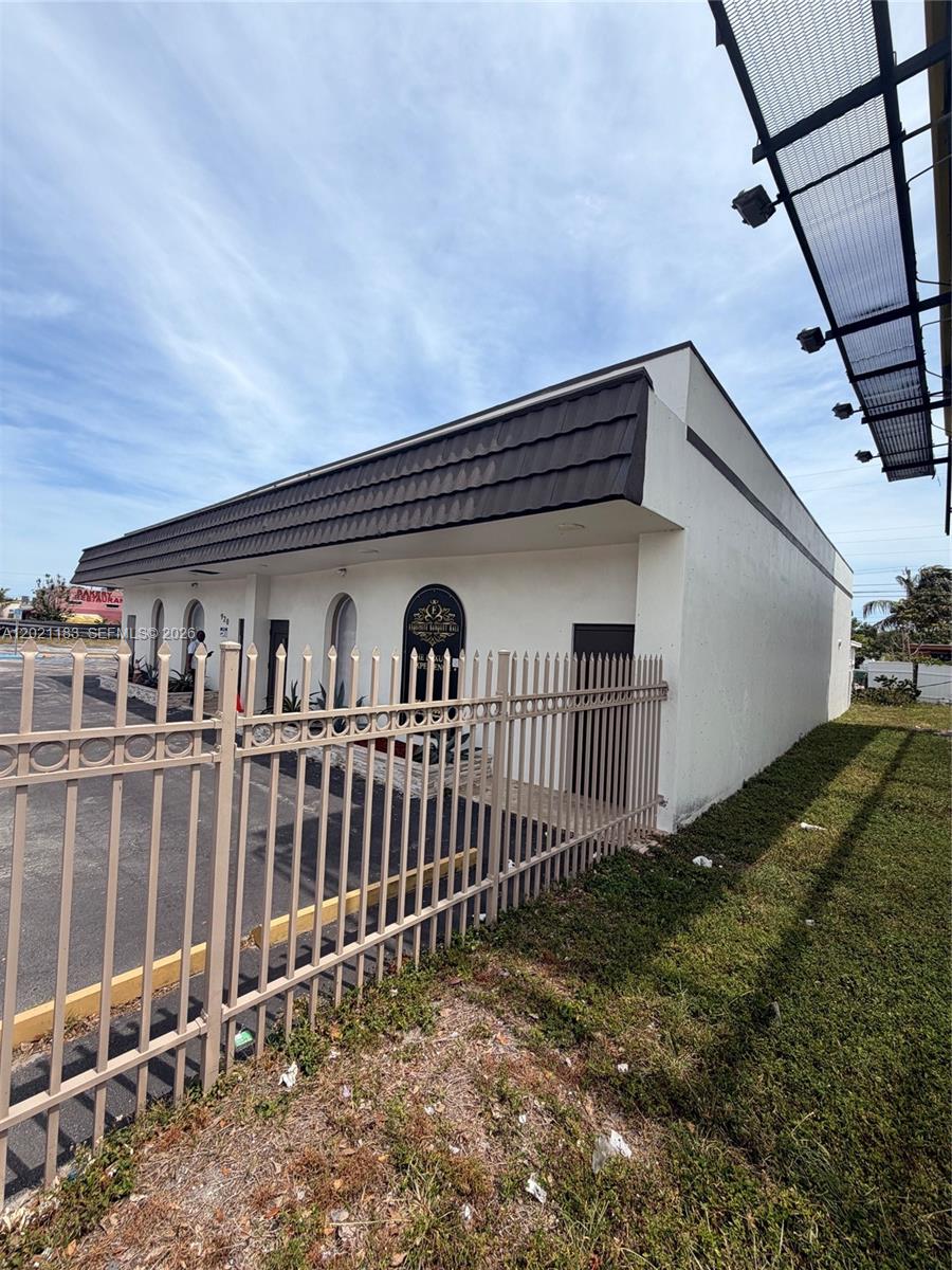 A low-rise commercial building with a dark mansard roof behind a metal security fence — 920 NW 119th St, Miami FL 33168, MIAMI, FL