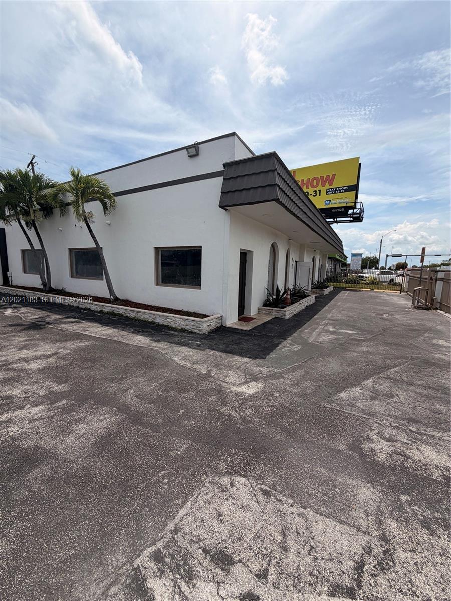 A white commercial building with palm trees and a billboard stands above a paved lot — 920 NW 119th St, Miami FL 33168, MIAMI, FL