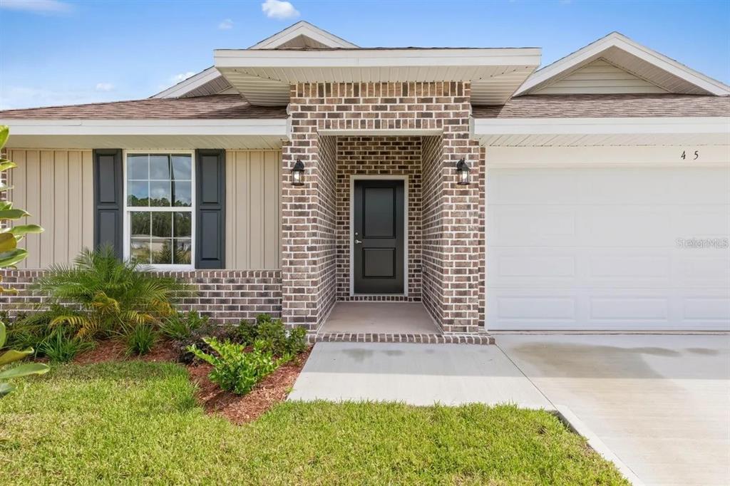 The exterior of a single-story house features a brick facade, a dark door, and garage — 45 BUNKER HILL DRIVE, PALM COAST, FL