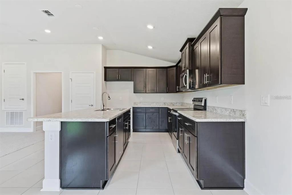 A kitchen features dark wood cabinets, light countertops, and a central island with a sink — 45 BUNKER HILL DRIVE, PALM COAST, FL