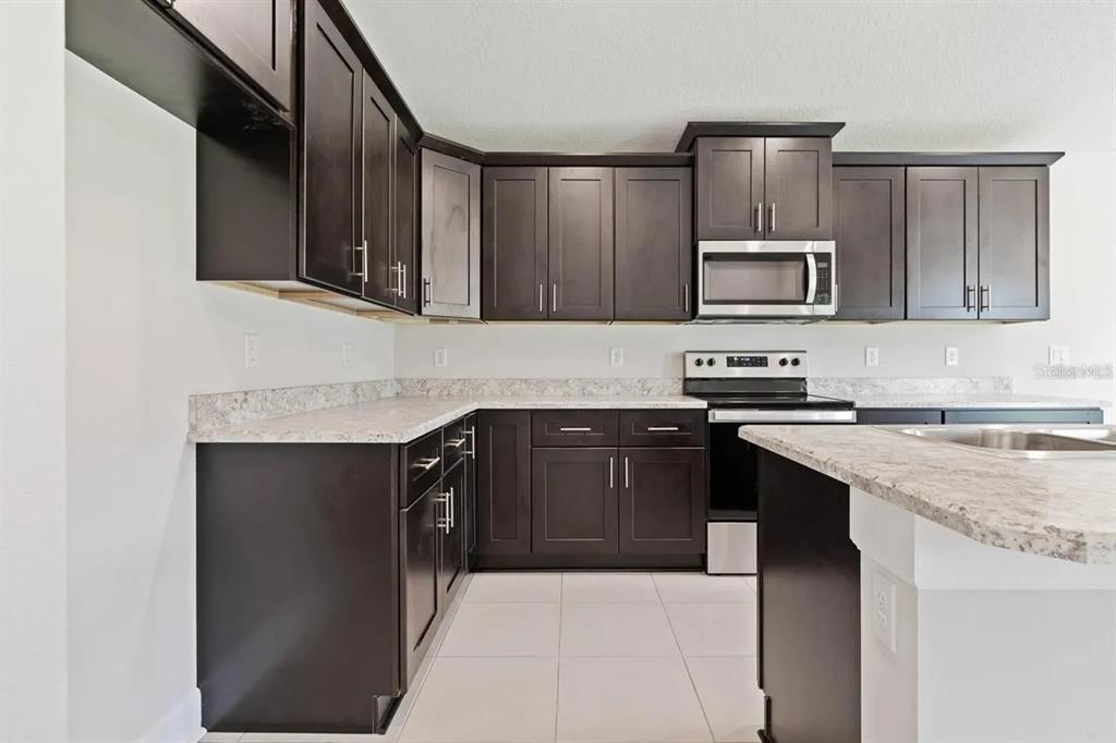 A kitchen features dark wood cabinets, light granite countertops, and stainless steel appliances — 45 BUNKER HILL DRIVE, PALM COAST, FL