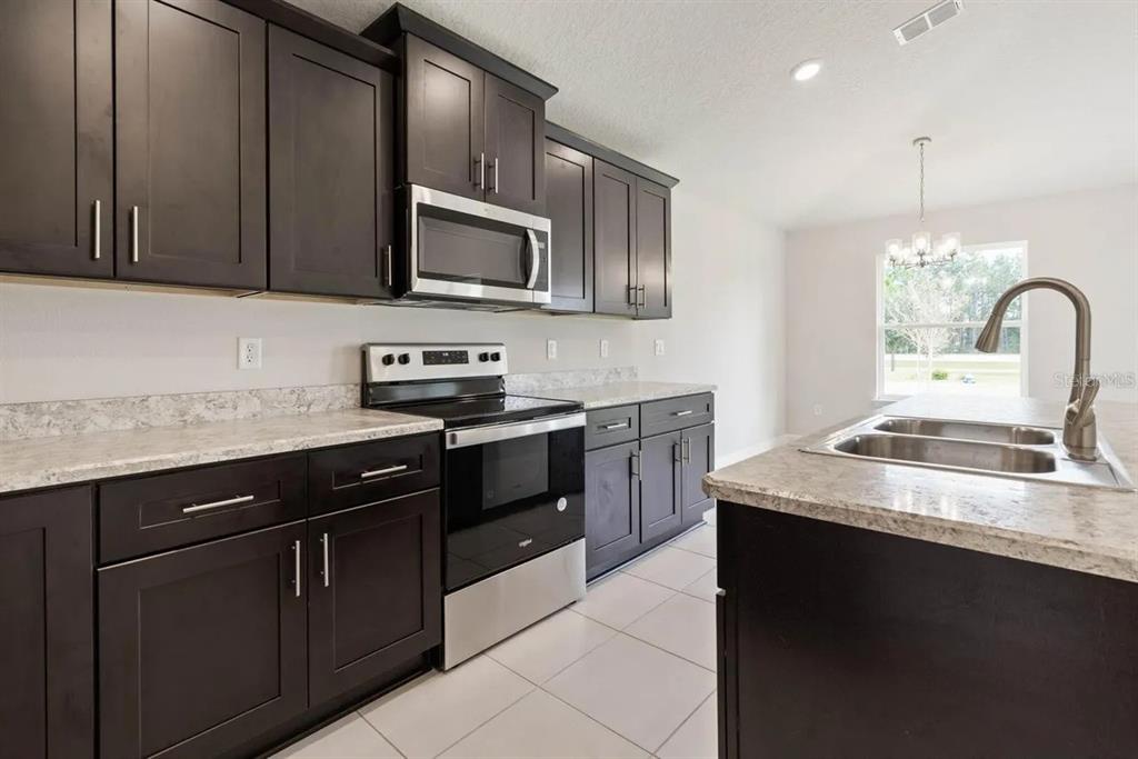 A kitchen with dark cabinets, stainless steel appliances, and a granite-topped island with a sink — 45 BUNKER HILL DRIVE, PALM COAST, FL
