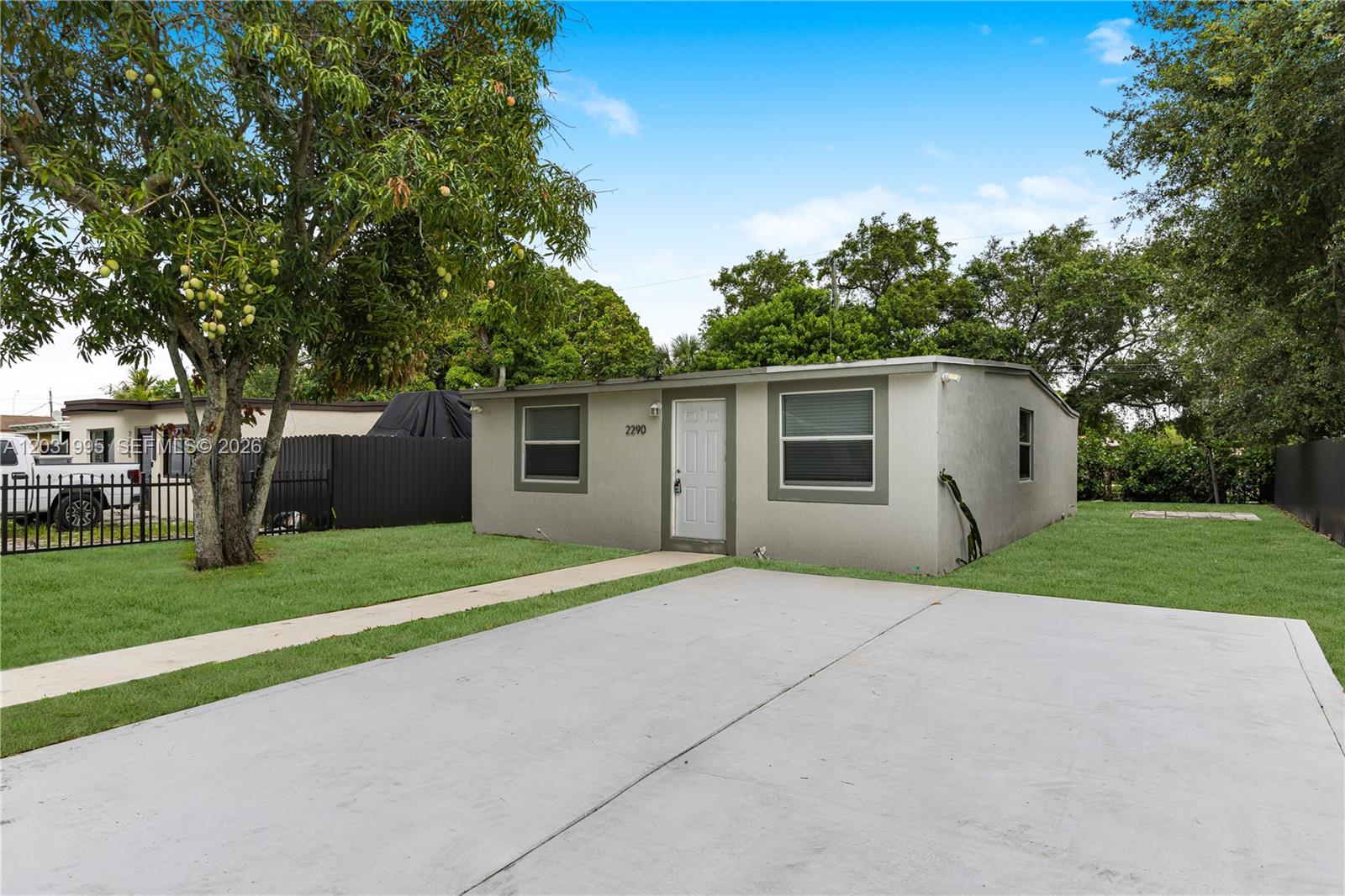 A single-story gray house with a concrete driveway and a large mango tree — 2290 Rutland St, Opa-Locka FL 33054, OPA-LOCKA, FL