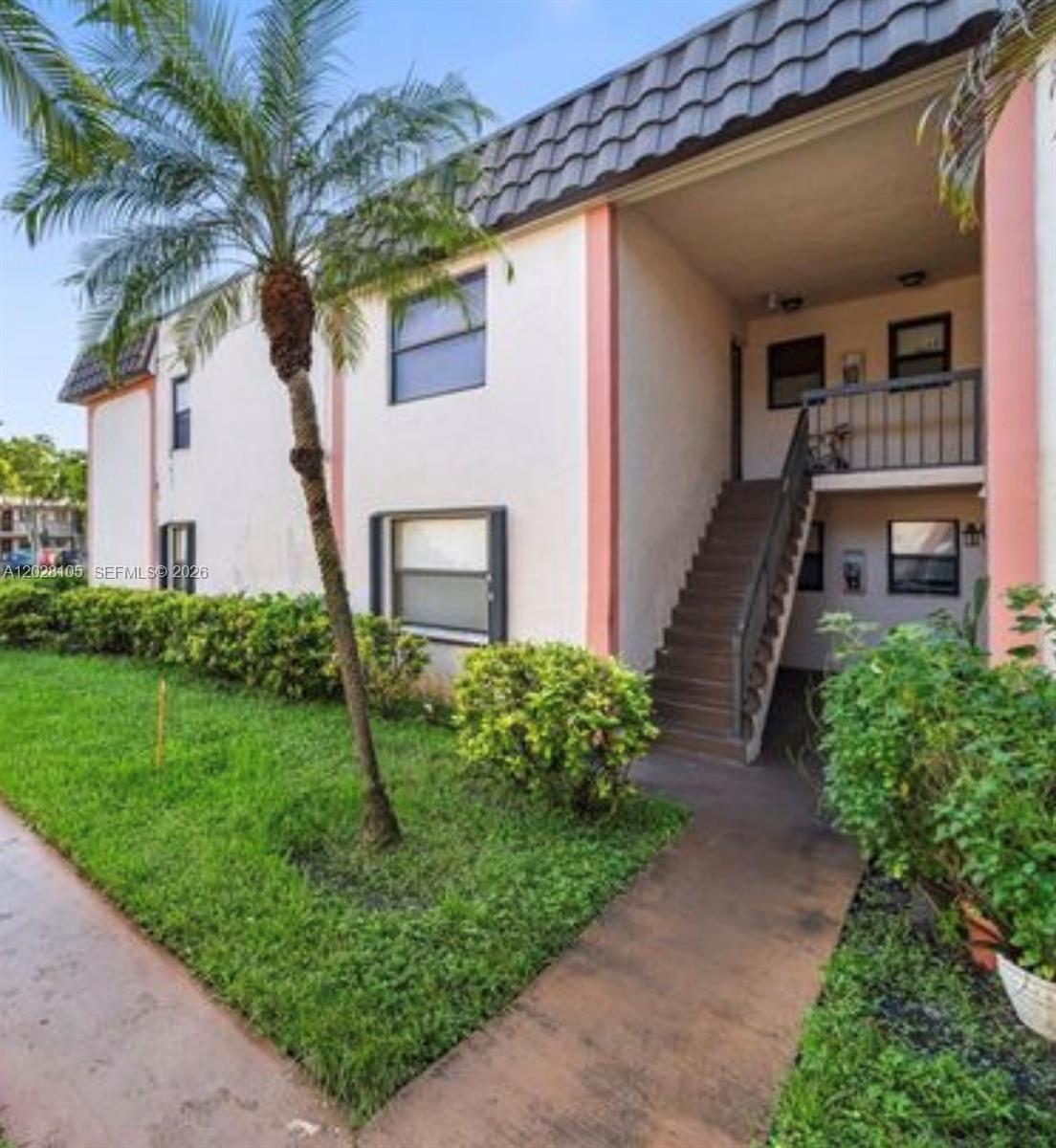 An exterior view of a two-story apartment building with a staircase and a palm tree — 851 NE 207th Ter # 103, Miami FL 33179, MIAMI, FL