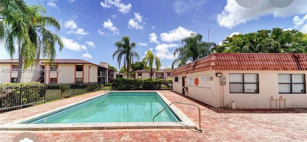 A rectangular swimming pool sits on a paved patio next to a low-rise apartment building — 851 NE 207th Ter # 103, Miami FL 33179, MIAMI, FL