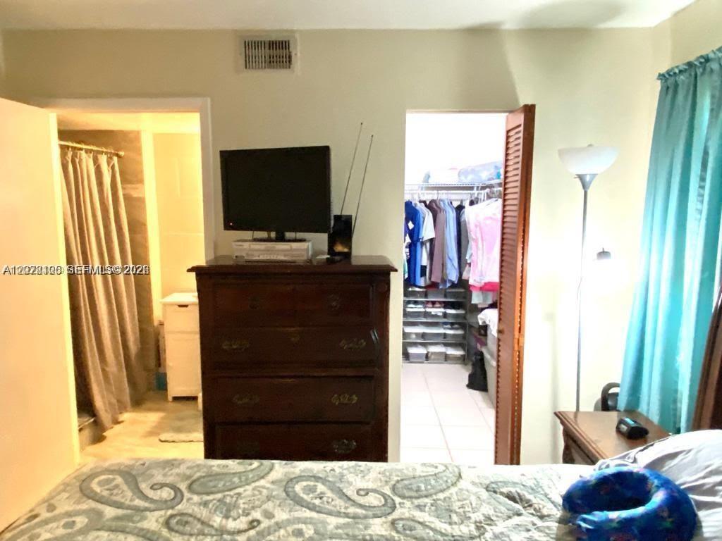 A bedroom features a dark wood dresser, a television, and doorways to a closet and bathroom — 851 NE 207th Ter # 103, Miami FL 33179, MIAMI, FL