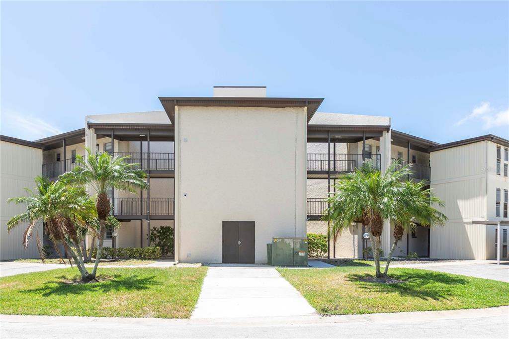 A three-story apartment building with a central entrance, balconies, and palm trees in the foreground — 5245 AMULET DRIVE UNIT 108, NEW PORT RICHEY, FL