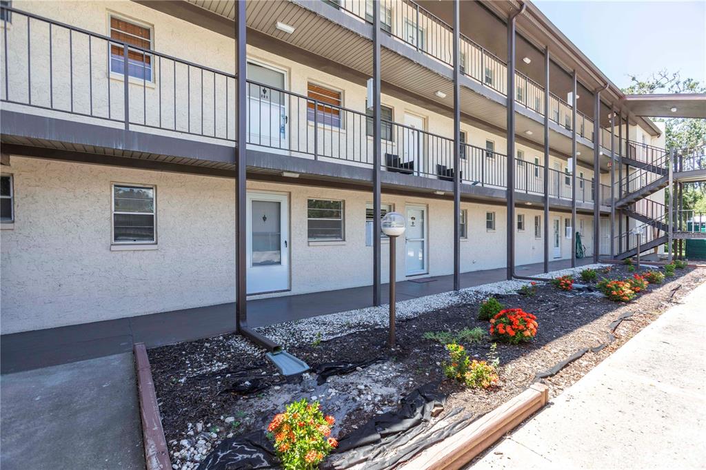 An exterior view of a multi-story apartment building with balconies and a landscaped garden bed — 5245 AMULET DRIVE UNIT 108, NEW PORT RICHEY, FL