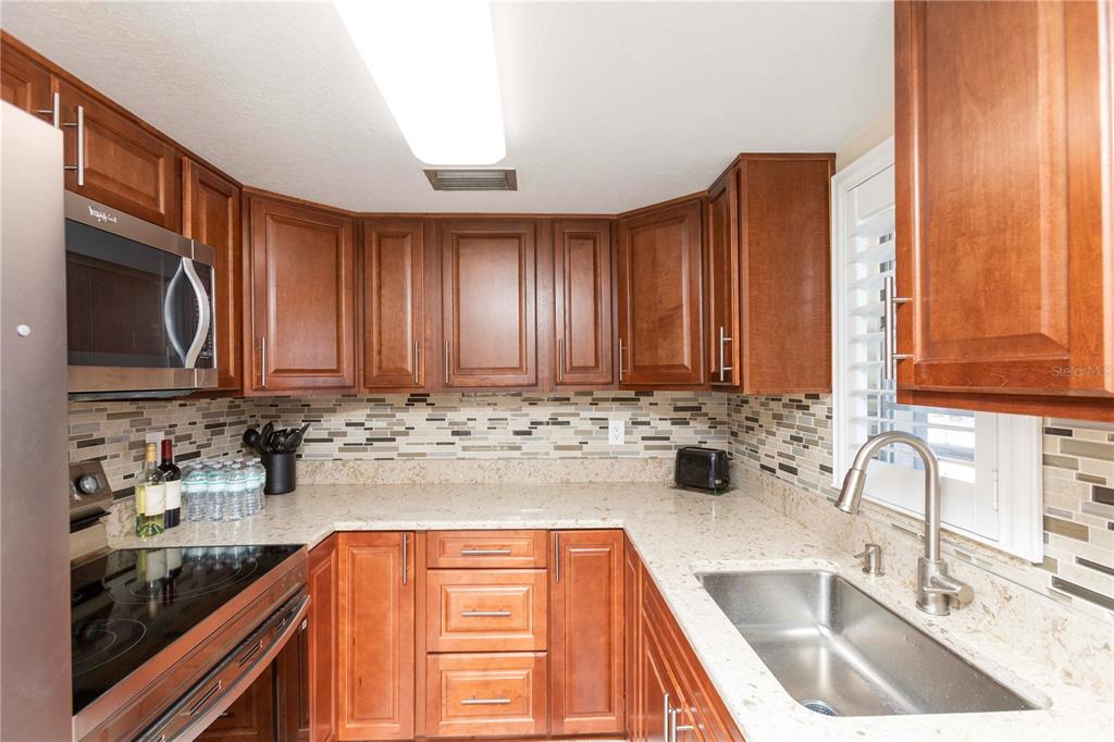 A kitchen with wood cabinets, granite countertops, a stainless steel sink, and a tiled backsplash — 5245 AMULET DRIVE UNIT 108, NEW PORT RICHEY, FL