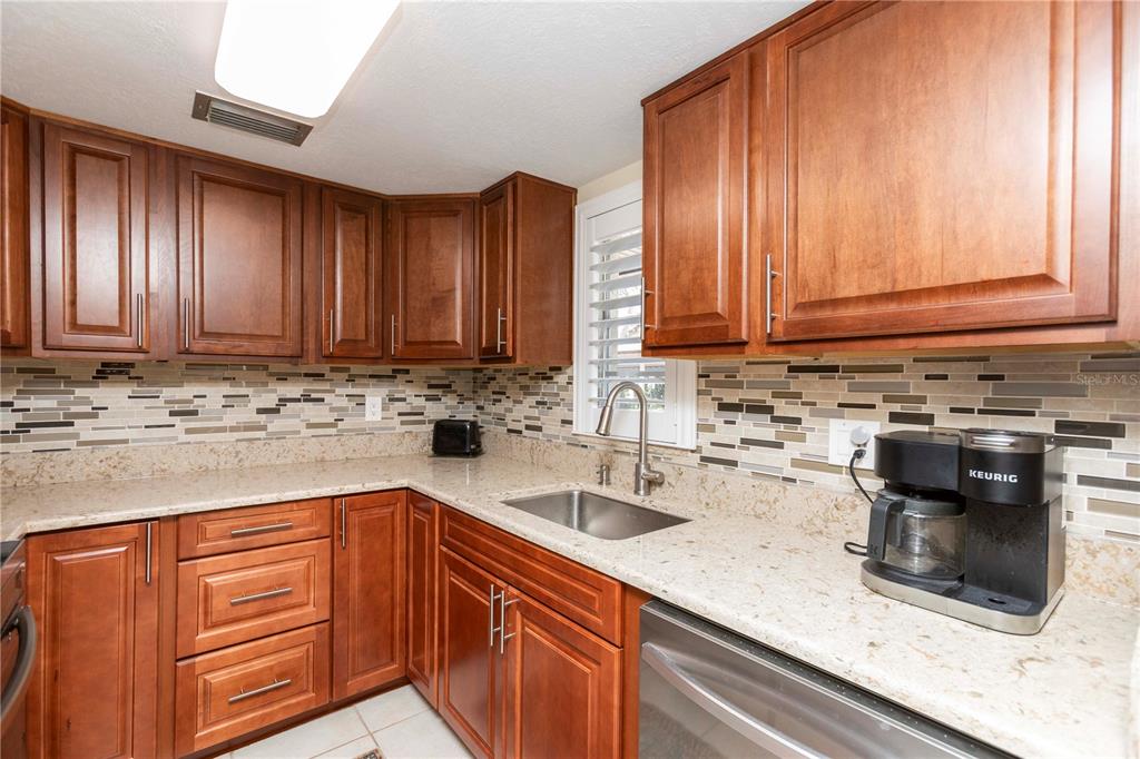 A kitchen with wood cabinets, granite countertops, a tiled backsplash, and stainless steel appliances — 5245 AMULET DRIVE UNIT 108, NEW PORT RICHEY, FL