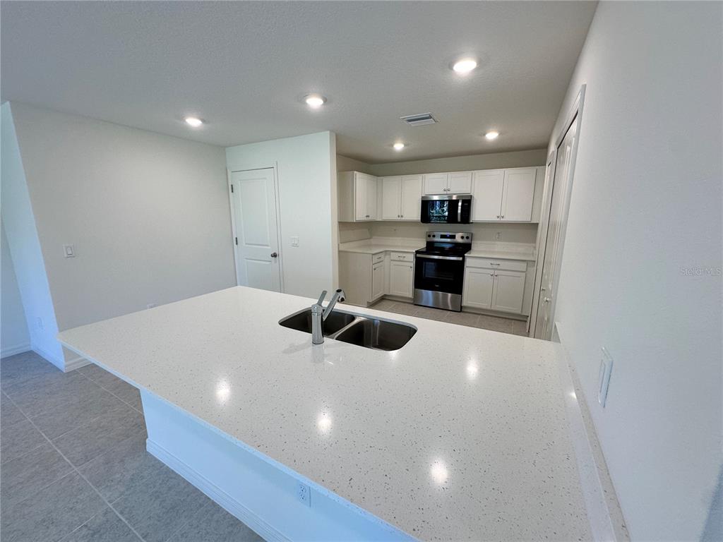 A kitchen features white cabinets, stainless steel appliances, and a large quartz-topped island with sink — 41 ROUND TREE DRIVE, PALM COAST, FL