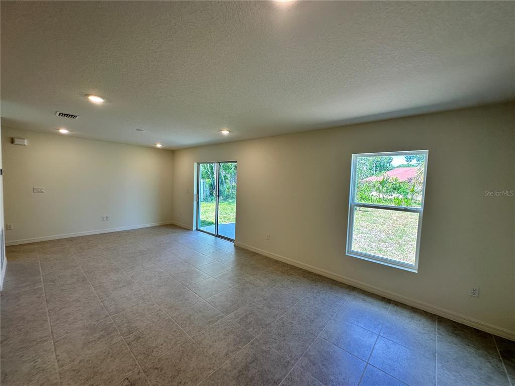An empty living room features light-colored tile flooring, recessed lighting, a sliding glass door, and windows — 41 ROUND TREE DRIVE, PALM COAST, FL