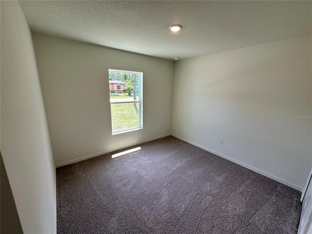 An empty bedroom features beige walls, gray carpeting, and a single window — 41 ROUND TREE DRIVE, PALM COAST, FL