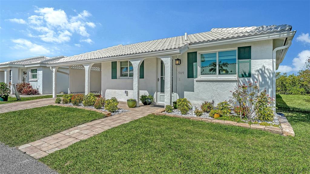 A white single-story house features a tiled roof, green shutters, and a paved walkway — 909 SPANISH DRIVE N, LONGBOAT KEY, FL