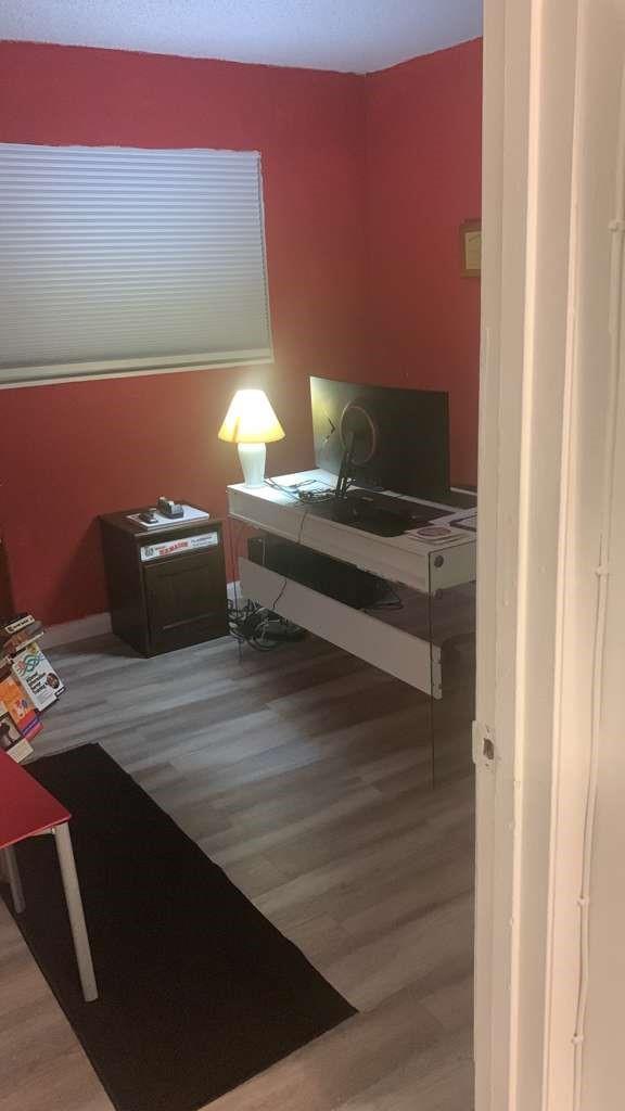 A home office with red walls, light wood-look flooring, a white desk, and a lamp — 1333 S Dixie Highway # 202, Deerfield Beach FL 33441, DEERFIELD BEACH, FL