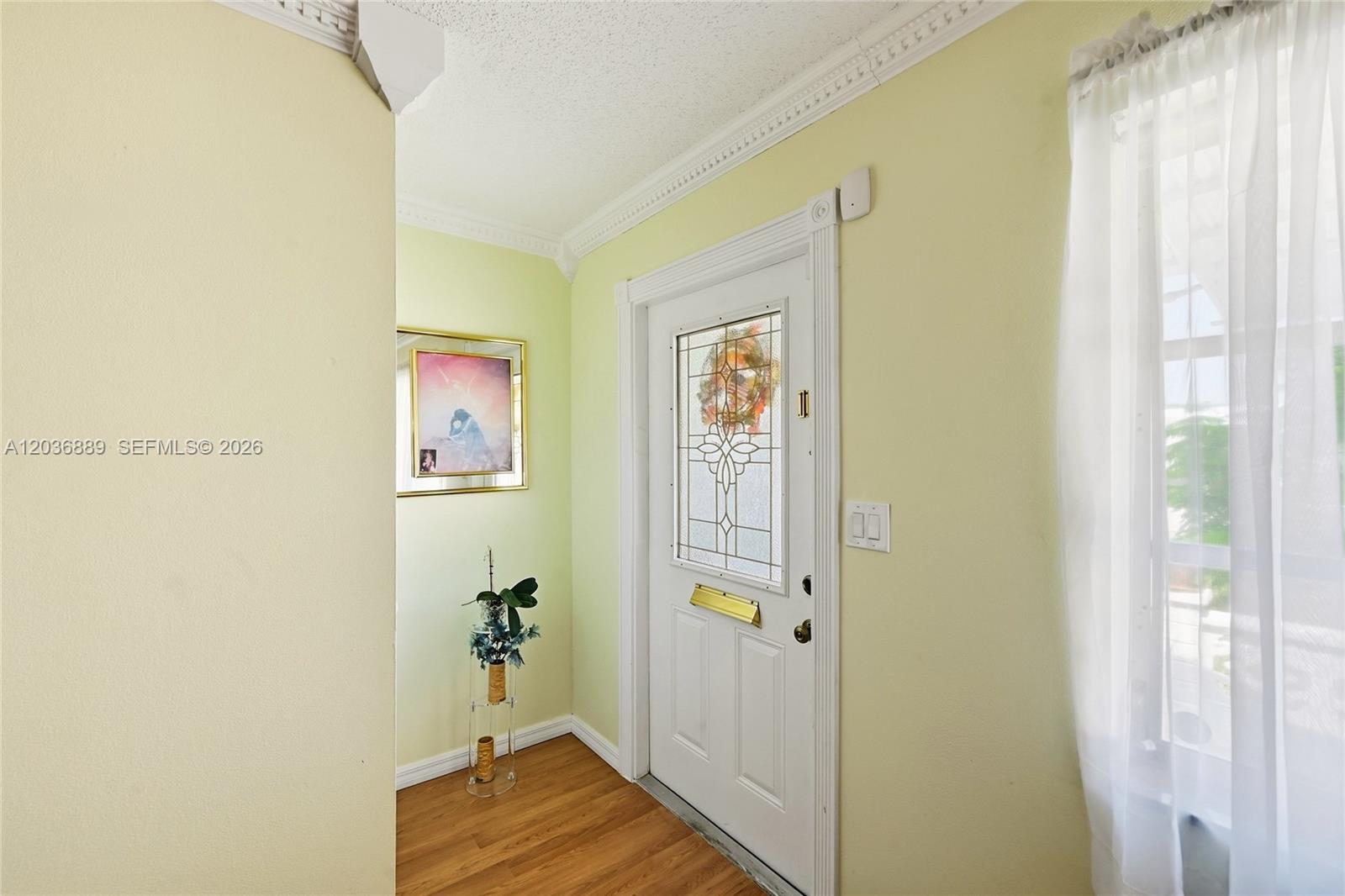 This entryway features light yellow walls, wood-look flooring, and a white door with glass — 1702 SW 22nd St, Boynton Beach FL 33426, BOYNTON BEACH, FL