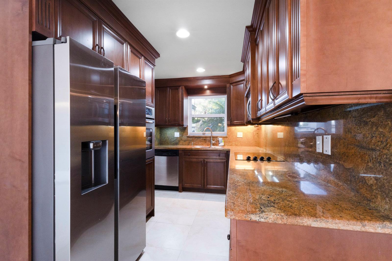 A kitchen features dark wood cabinets, granite countertops, stainless steel appliances, and light tile flooring — 2940 NE 18th Street, Pompano Beach FL 33062, POMPANO BEACH, FL