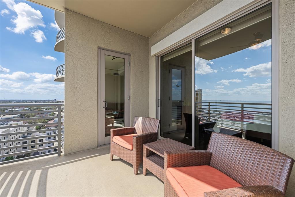 A balcony with wicker chairs and orange cushions overlooks a city and water view — 275 BAYSHORE BOULEVARD UNIT 1507, TAMPA, FL