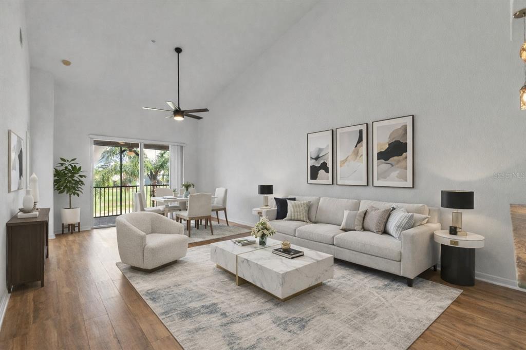 A living room with a vaulted ceiling, white sofa, marble coffee tables, and a dining area — 819 FAIRWAYCOVE LANE UNIT 203, BRADENTON, FL