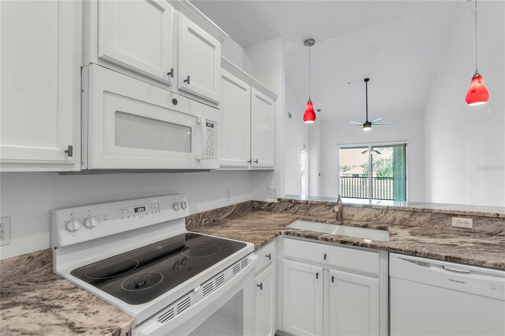 A kitchen features white cabinetry, granite countertops, a white electric stove, and two red pendants — 819 FAIRWAYCOVE LANE UNIT 203, BRADENTON, FL