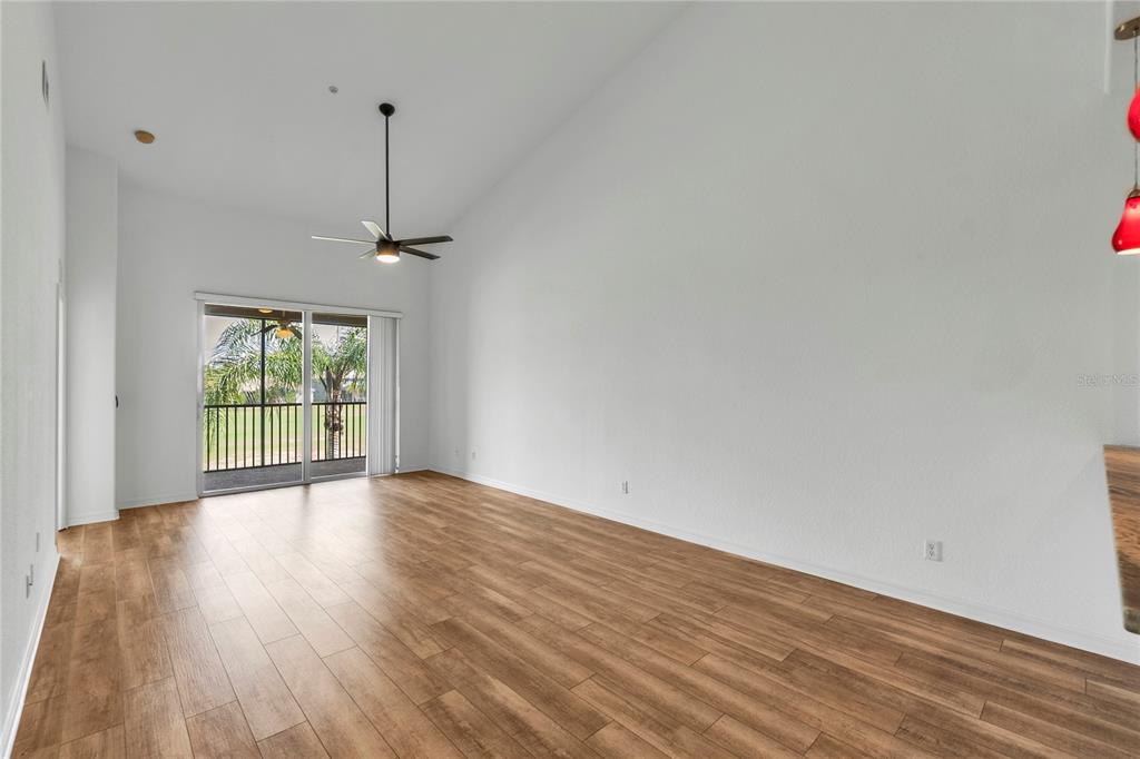 A spacious living room with vaulted ceilings, wood-look flooring, and a sliding glass door — 819 FAIRWAYCOVE LANE UNIT 203, BRADENTON, FL