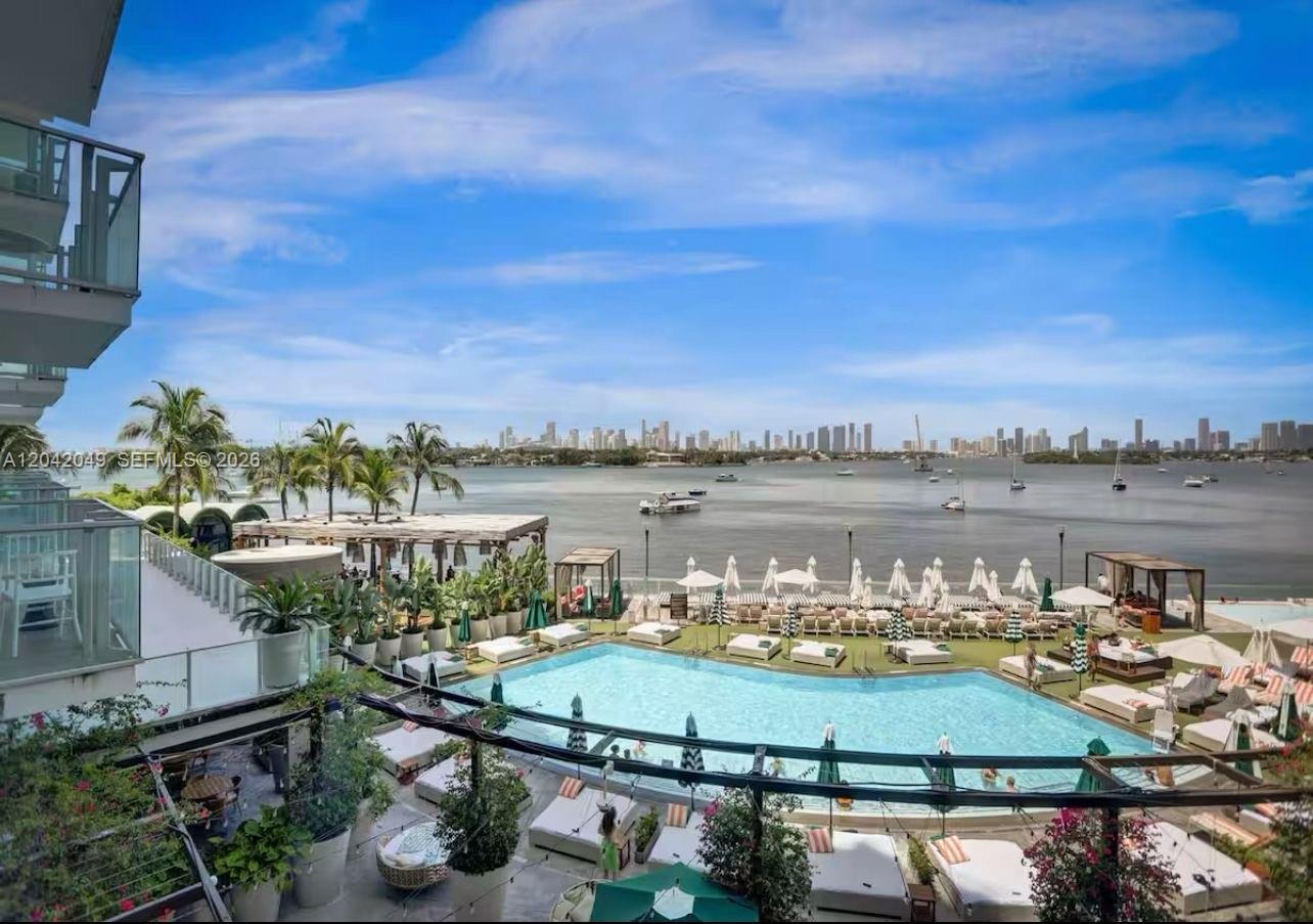An elevated view of a swimming pool overlooking a bay with a distant city skyline — 1100 West Ave # 1007, Miami Beach FL 33139, MIAMI BEACH, FL