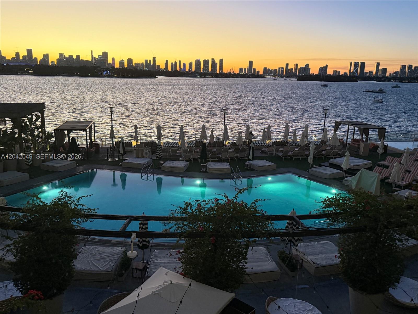 A swimming pool overlooks a bay with a city skyline visible at sunset — 1100 West Ave # 1007, Miami Beach FL 33139, MIAMI BEACH, FL