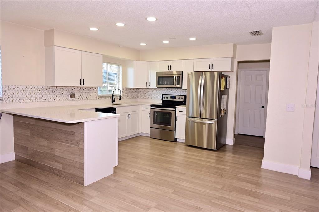A kitchen with white cabinets, stainless steel appliances, and a wood-look peninsula island — 306 FERN ROAD, WINTER HAVEN, FL