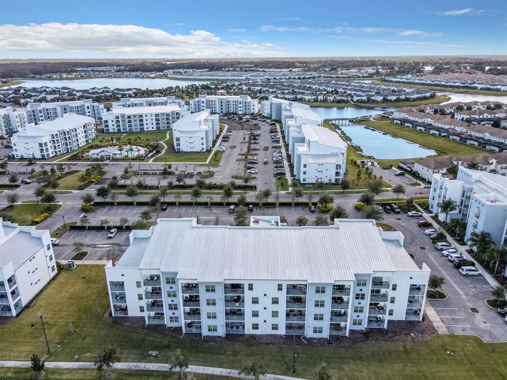 An aerial view shows a multi-story white apartment building with a metal roof and parking — 4741 CLOCK TOWER DRIVE UNIT 108, KISSIMMEE, FL