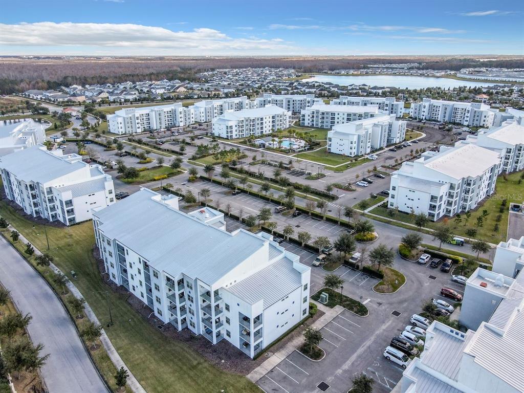 An aerial view shows multiple white apartment buildings surrounded by parking lots and landscaping — 4741 CLOCK TOWER DRIVE UNIT 108, KISSIMMEE, FL