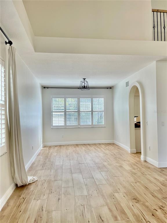 An empty room features light wood-look tile flooring, a large window with shutters, and an archway — 13261 ROYAL GEORGE AVENUE, ODESSA, FL