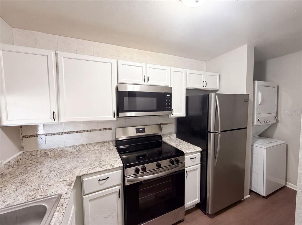 A kitchen features white cabinets, granite-look countertops, stainless steel appliances, and a stacked laundry unit — 5213 VIA HACIENDA CIRCLE UNIT 307, ORLANDO, FL