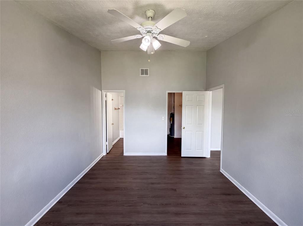 A room with gray walls, dark wood-look flooring, a ceiling fan, and two open doorways — 5213 VIA HACIENDA CIRCLE UNIT 307, ORLANDO, FL