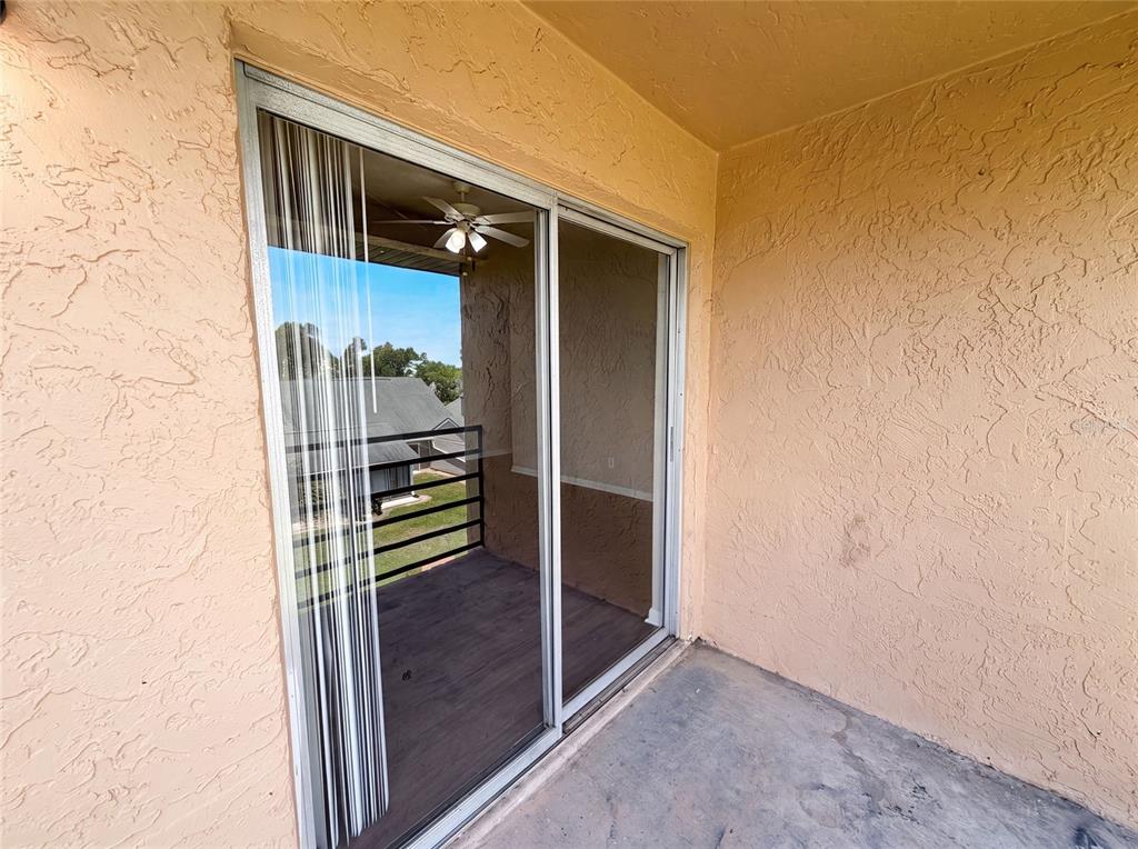 A covered balcony features a sliding glass door, textured peach walls, and a concrete floor — 5213 VIA HACIENDA CIRCLE UNIT 307, ORLANDO, FL