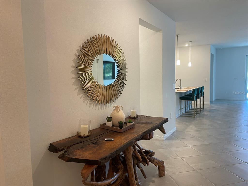A live-edge wood console table sits beneath a sunburst mirror in a tiled entryway — 11308 PINOT DRIVE, VENICE, FL