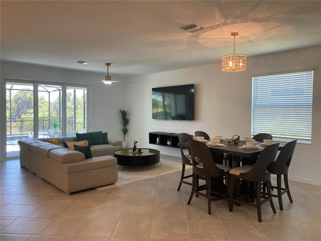 An open-concept living and dining area features tile flooring, a sectional sofa, and a television — 11308 PINOT DRIVE, VENICE, FL