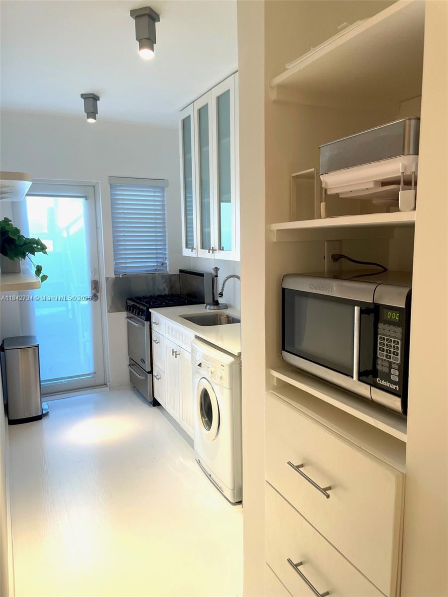 A galley kitchen features white cabinetry, a built-in microwave, and a front-loading washing machine — 1616 Euclid Ave # 14, Miami Beach FL 33139, MIAMI BEACH, FL