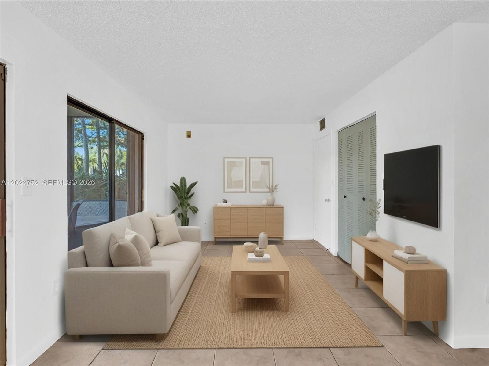 This living room features a beige sofa, a wooden coffee table, and a wall-mounted television — 831 NE 199th St # 34, Miami FL 33179, MIAMI, FL