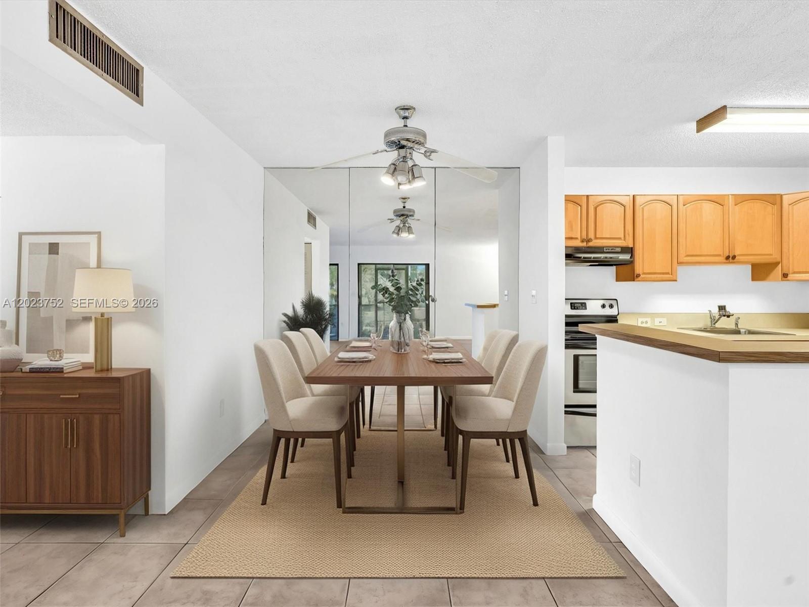 A dining area features a wooden table, upholstered chairs, a mirrored wall, and adjacent kitchen — 831 NE 199th St # 34, Miami FL 33179, MIAMI, FL