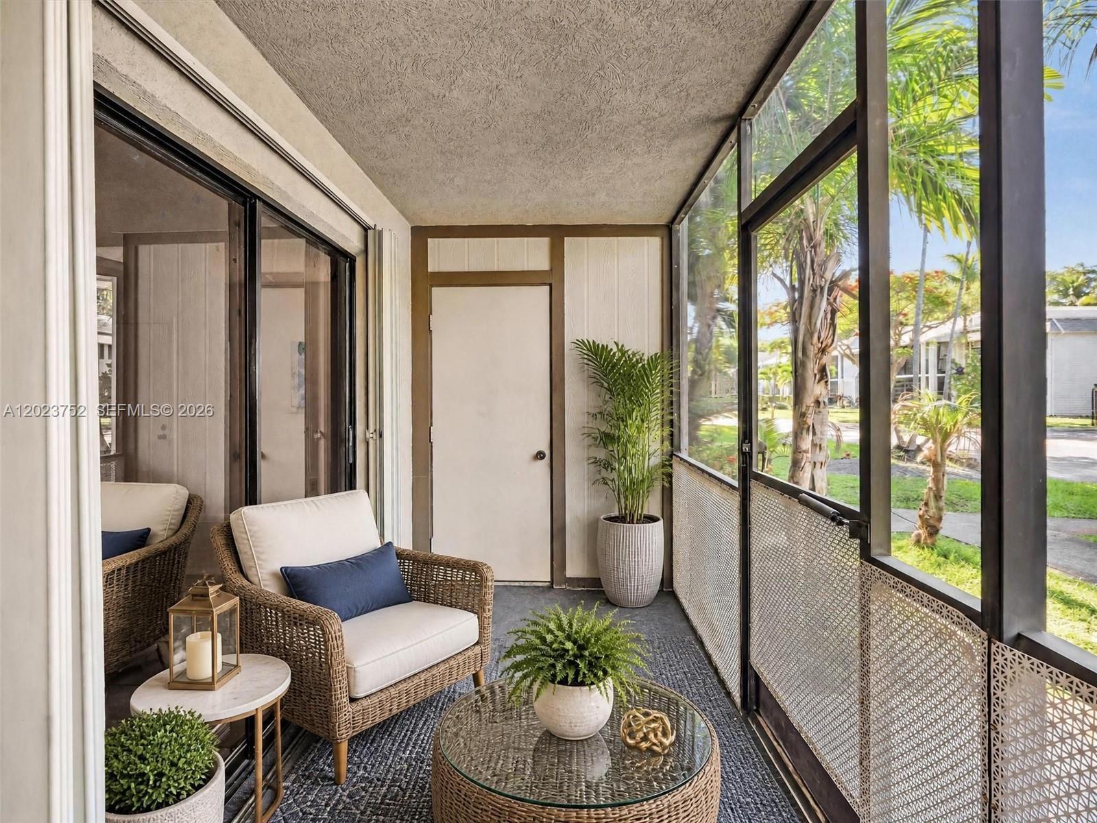 A screened-in porch features wicker furniture, a glass-topped coffee table, and views of palm trees — 831 NE 199th St # 34, Miami FL 33179, MIAMI, FL
