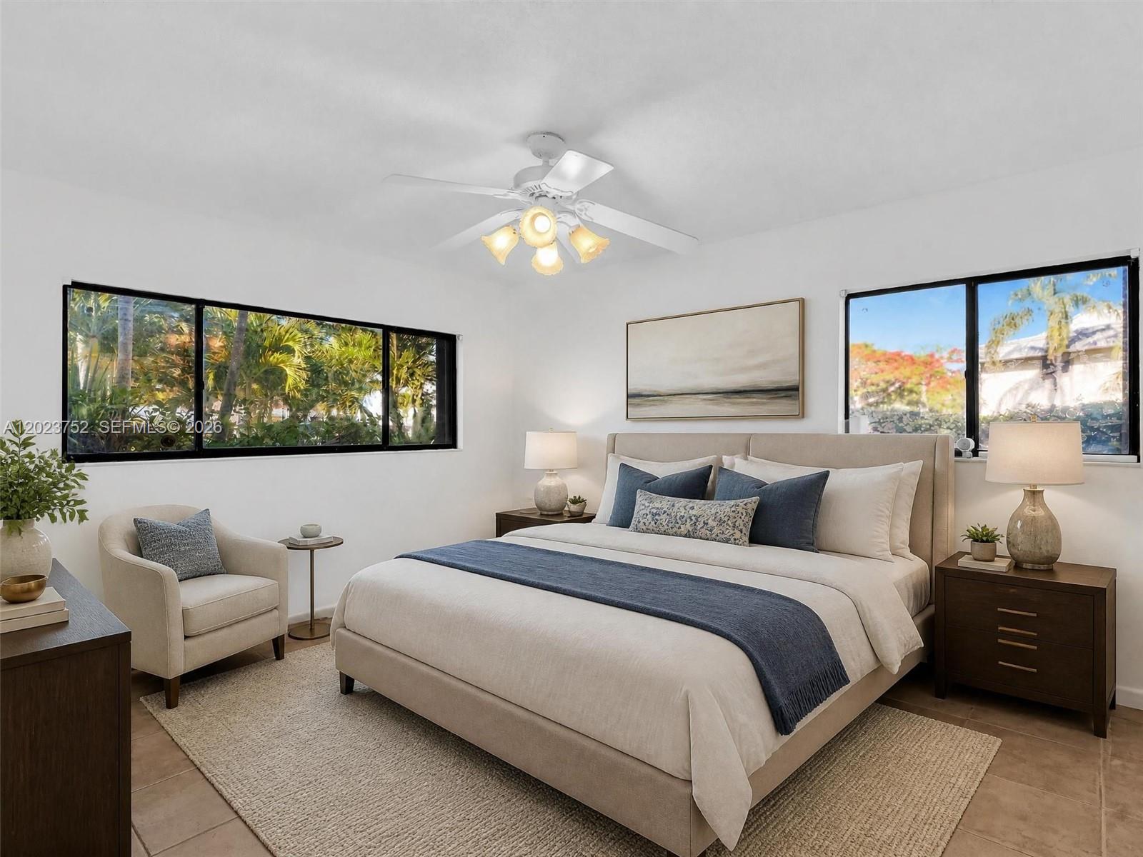 A bedroom features a bed, two nightstands, an armchair, and windows overlooking tropical greenery — 831 NE 199th St # 34, Miami FL 33179, MIAMI, FL