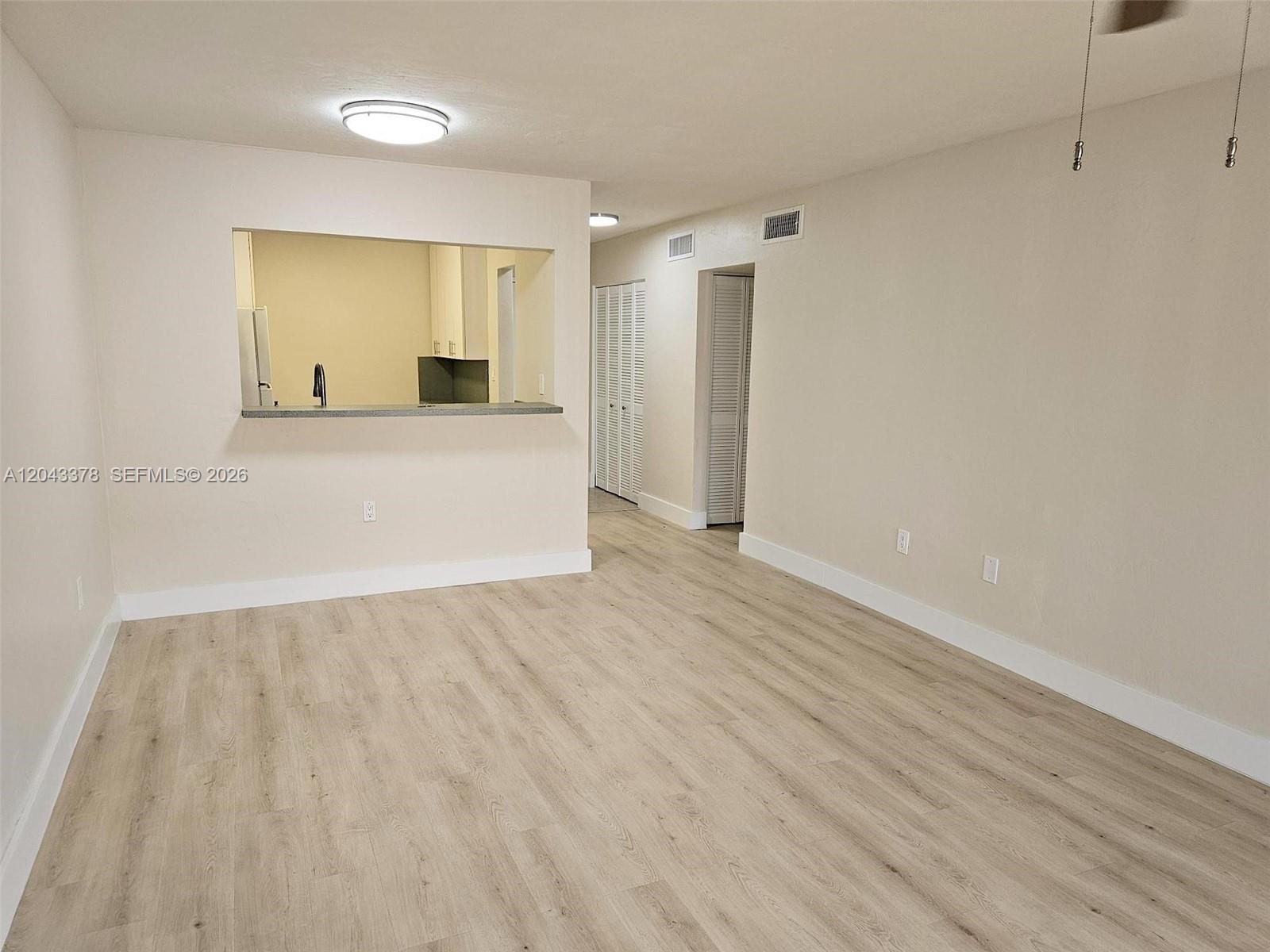 This living room features light wood-look flooring, neutral walls, and a kitchen pass-through window — 11223 SW 88th St # 216C, Miami FL 33176, MIAMI, FL