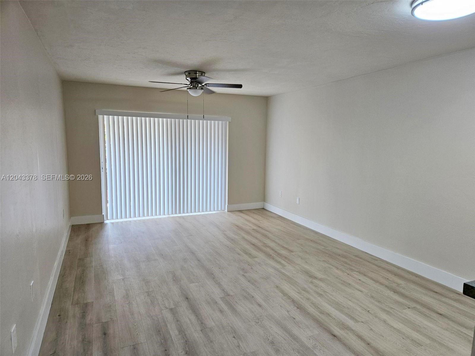 An empty room features light wood-look flooring, beige walls, a ceiling fan, and vertical blinds — 11223 SW 88th St # 216C, Miami FL 33176, MIAMI, FL