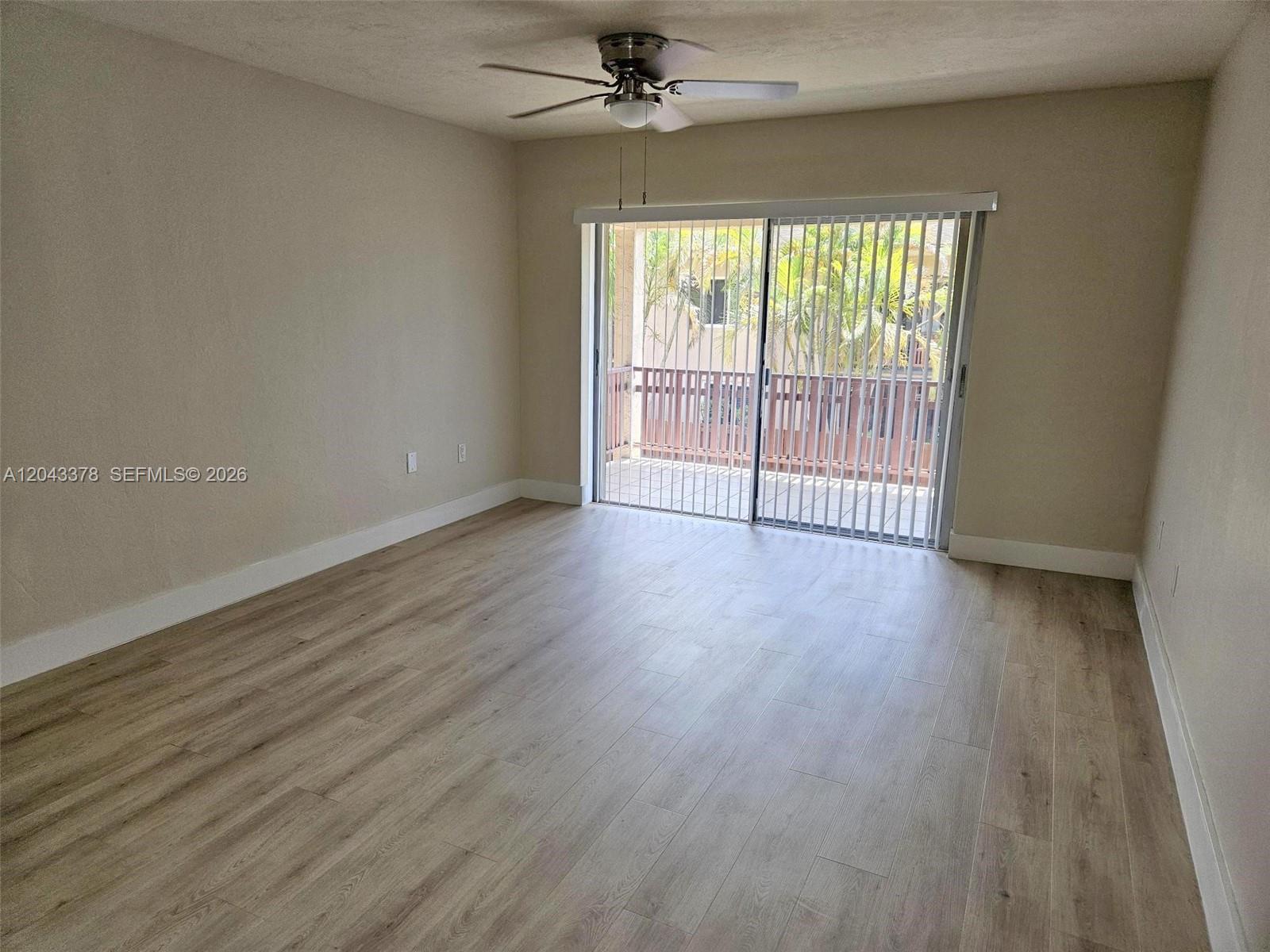An empty room features light wood-look flooring, a ceiling fan, and sliding glass balcony doors — 11223 SW 88th St # 216C, Miami FL 33176, MIAMI, FL