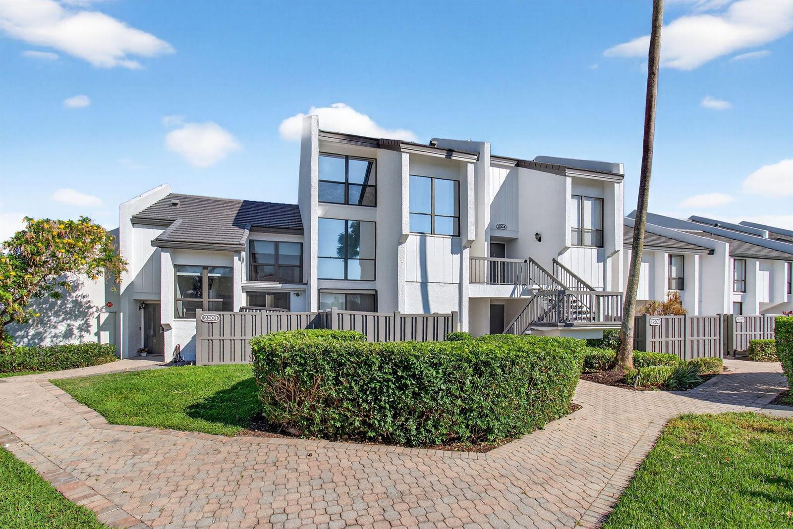 A multi-story residential building with white stucco walls, dark roof tiles, and a paved walkway — 2303 Bridgewood Drive # 2303, Boca Raton FL 33434, BOCA RATON, FL